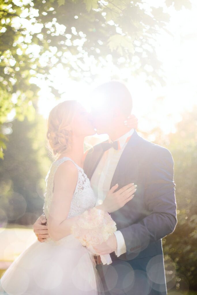 bride and groom kissing near tree against the sun photo