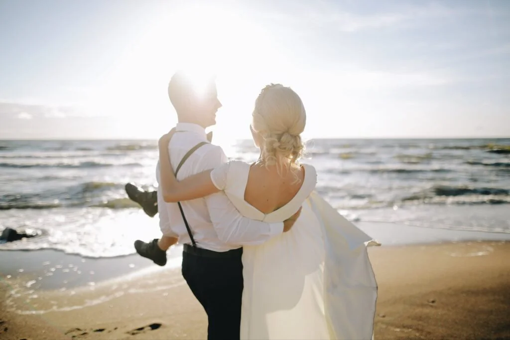 man lifting his new wife on the beach after a micro wedding