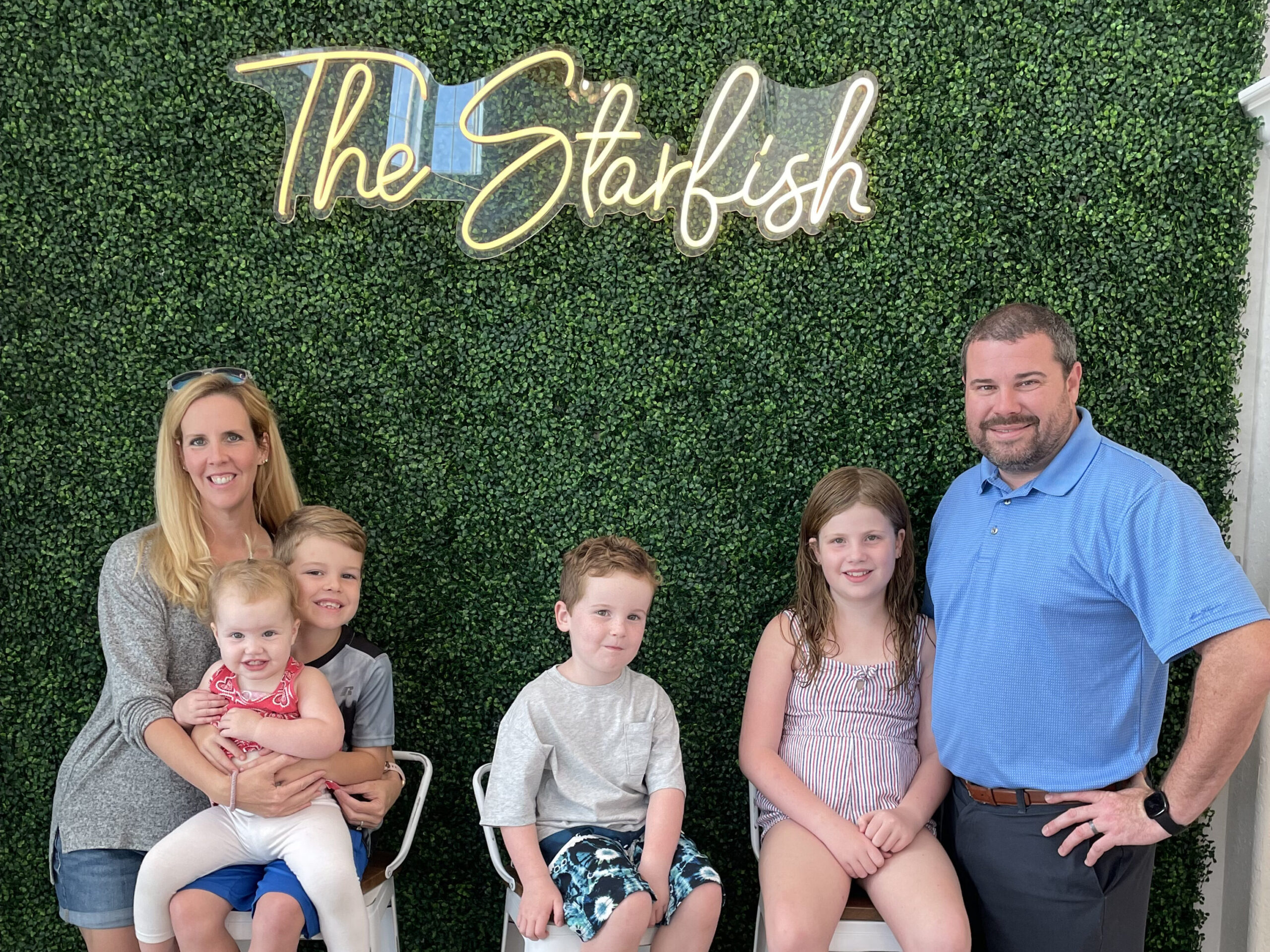 Family posing for a picture beneath a sign at a beach house vacation rental in surfside beach texas called Starfish Swim-up
